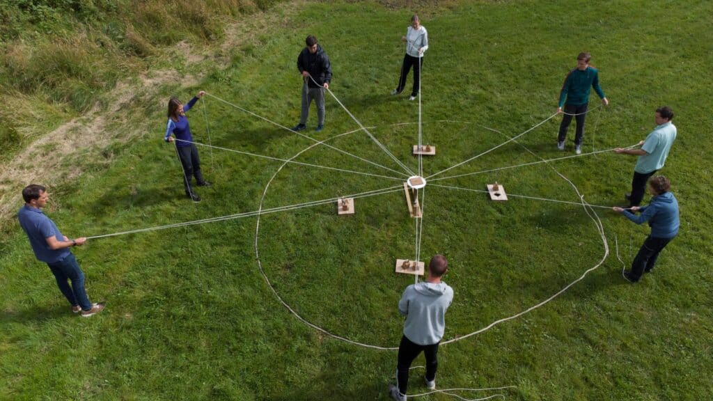 Utendørs teambuilding aktiv i naturen med flere deltakere som holder på tau rundt et sentralt punkt.