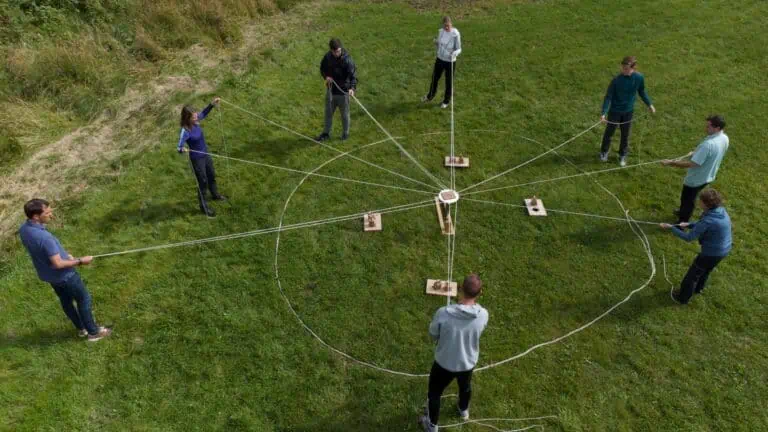 Utendørs teambuilding aktiv i naturen med flere deltakere som holder på tau rundt et sentralt punkt.