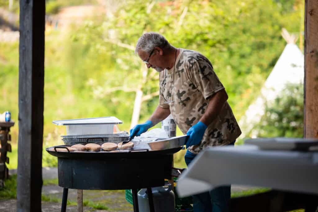 Detaljert bilde av mann som lager mat utendørs, med natur i bakgrunnen.